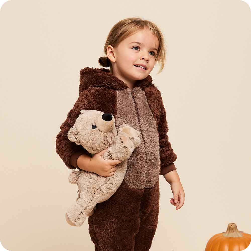 Child wearing a brown bear-themed outfit holding a teddy bear against a beige background