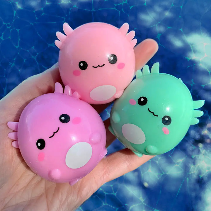 Three colorful axoloyl-like squish toys held in a hand against a blue sky background.