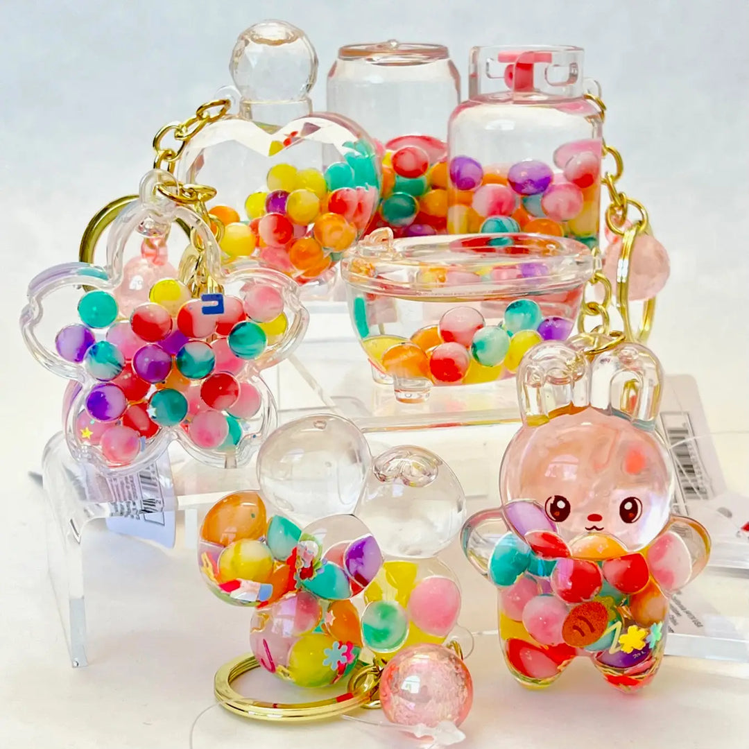 Colorful keychains with transparent containers filled with multicolored beads on a light background.