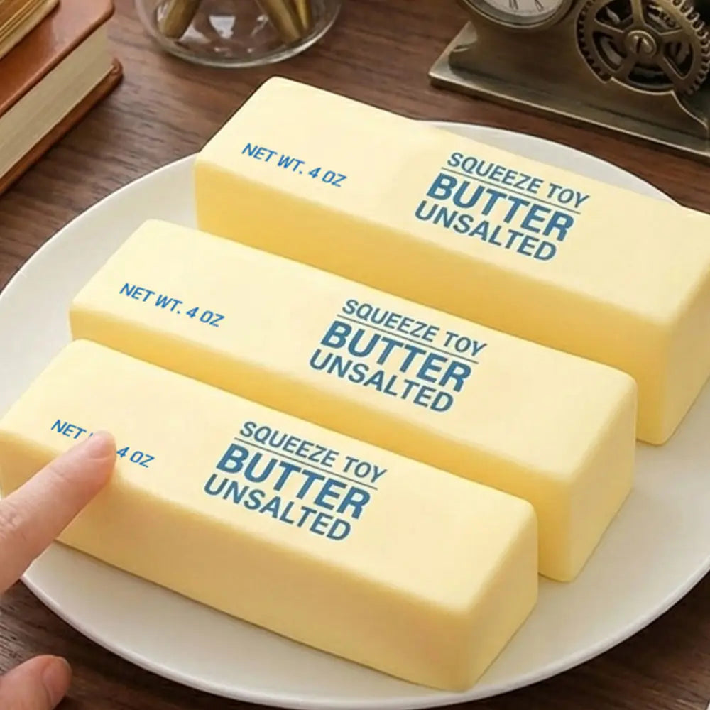 Three blocks of 'Squeeze Toy Butter Unsalted' on a plate with a hand touching one of them.