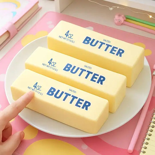 Three blocks of butter on a plate with a hand pointing at them, set against a colorful background.