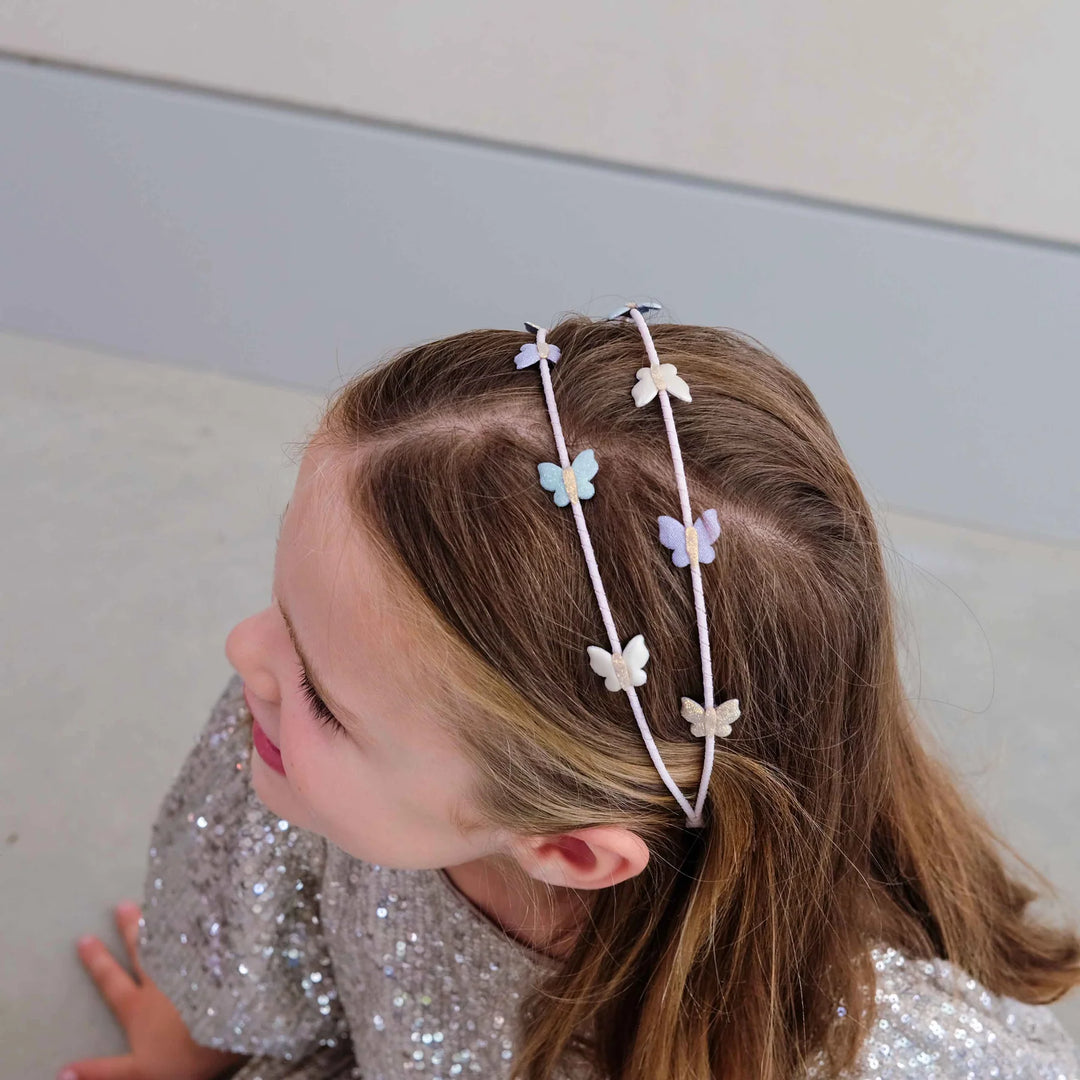 A young girl with brown hair wearing a double-strand white headband decorated with small pastel butterfly clips, shown in a close-up profile view.