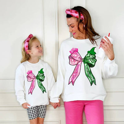 white sweatshirt with a big bow on it, one side of the bow is green like Elphaba and the other side is pink like Glinda. The sweatshirt is the theme of Wicked. 