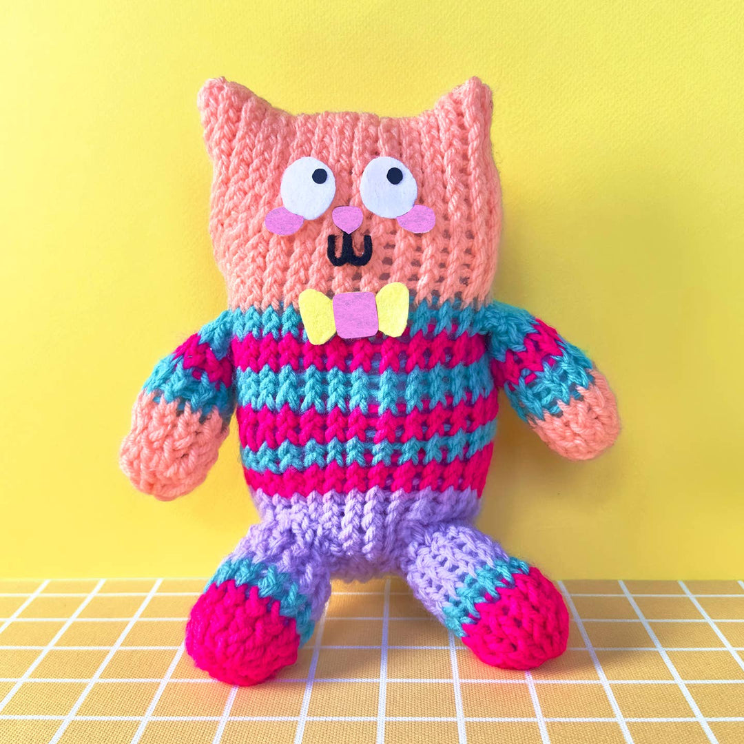Colorful knitted toy with a pink face and striped body on a yellow background