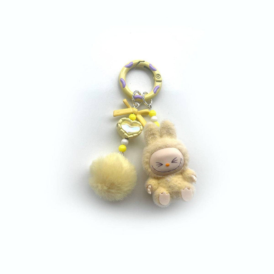 Plush keychain with a yellow pom-pom and labubu inspired charachter on a white background