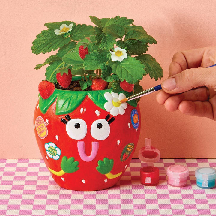 strawberry planter with plants coming out of the top. the planter is shaped like a strawberry with a happy face on it and a daisy. 