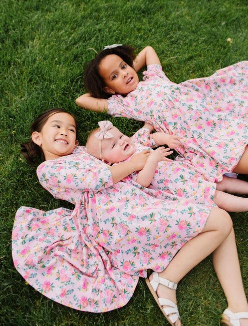 little girls laying on the grass showing the floral print and the skirts of the dresses laid out flat. 