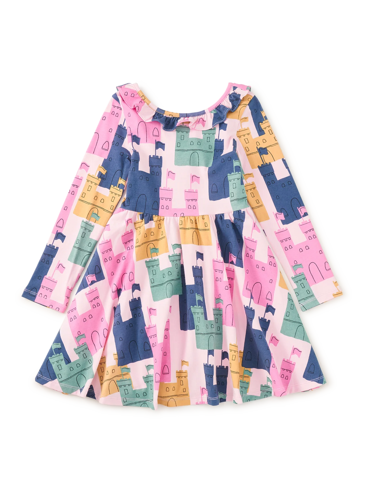 A long-sleeve children's dress with a colorful castle pattern in pink, navy blue, teal, and mustard yellow on a white background.