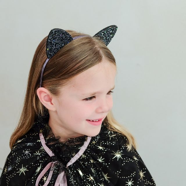 Child wearing a black glittery cat ear headband and star-patterned outfit on a plain background