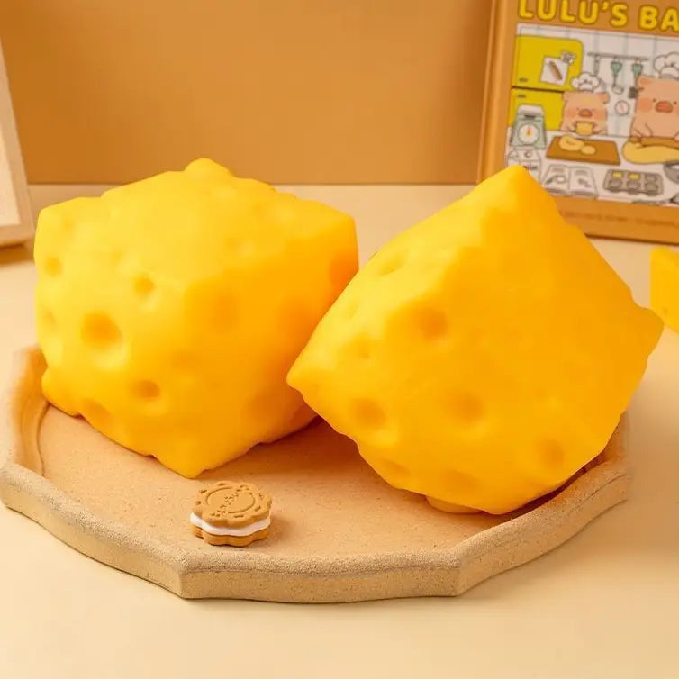 Two yellow cheese-shaped squish toys on a wooden board 