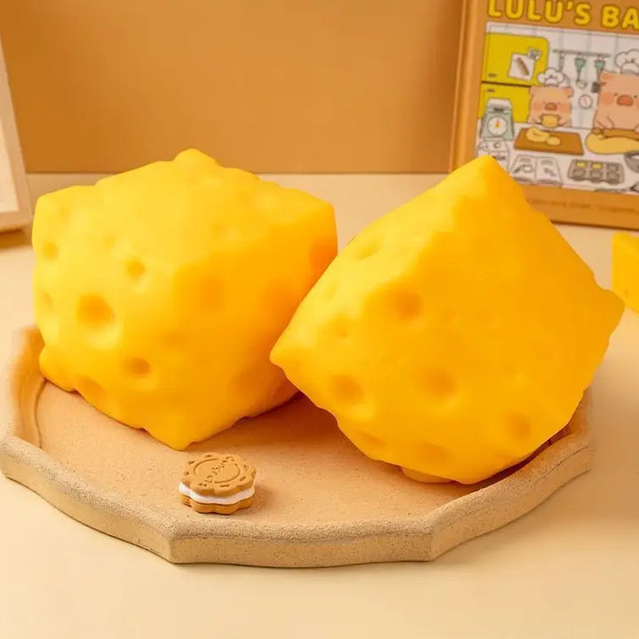 Two yellow cheese-shaped squish toys on a wooden board 
