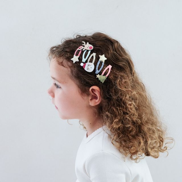 Child with curly hair wearing a colorful hair clip against a white background
