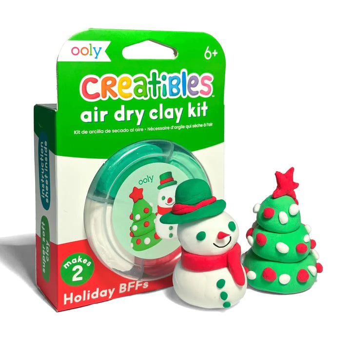 Ooly Creatibles Air Dry Clay Kit with a green and white retail box, shown next to two small holiday-themed clay figures: a snowman with a green hat and red scarf, and a green Christmas tree with red ornaments and a red star.