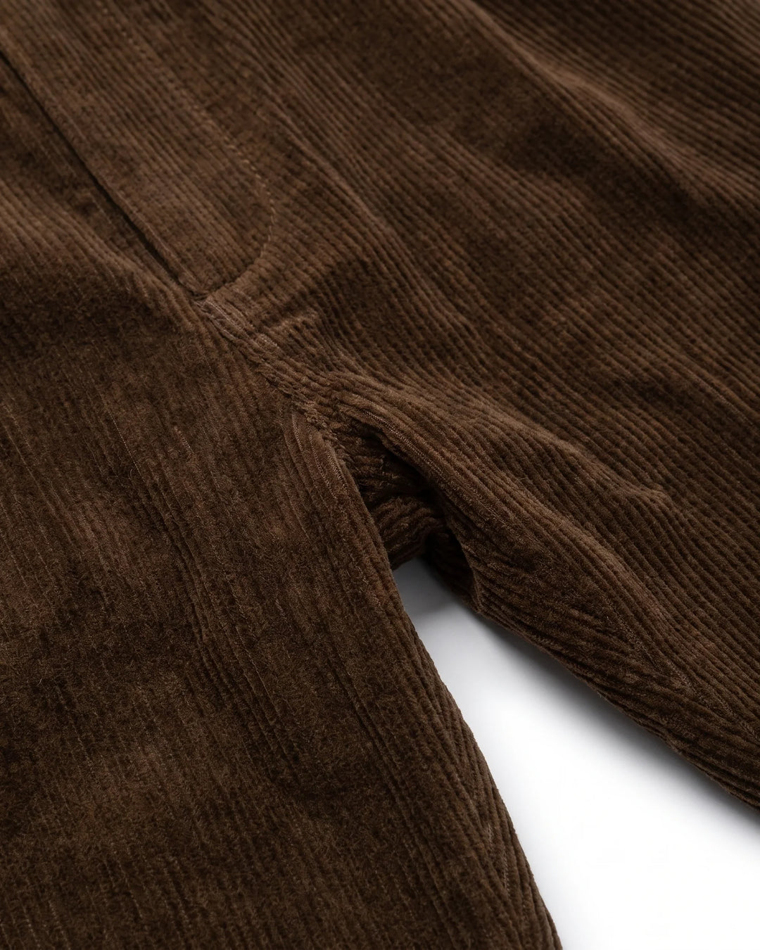 Close-up of dark brown corduroy fabric showing the ribbed texture and a fold over a white background.