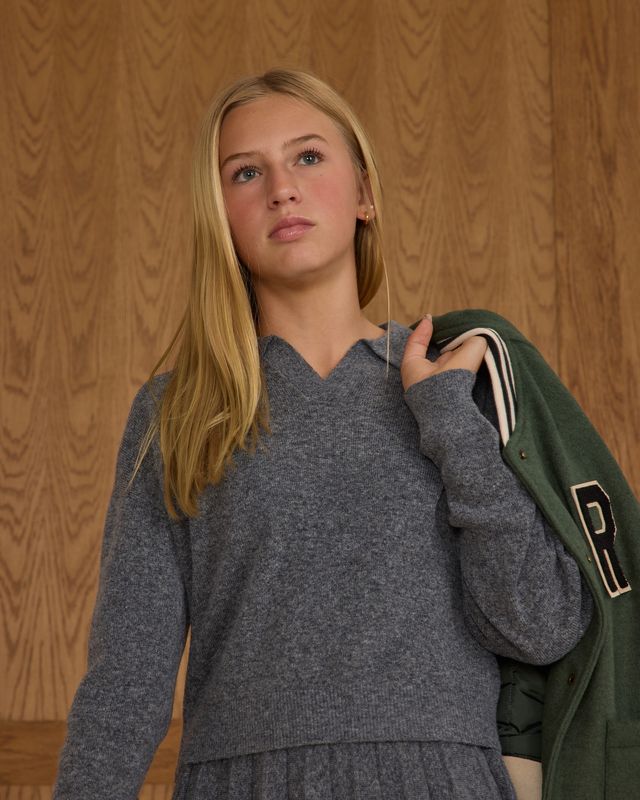 Woman in gray sweater holding a green jacket against a wooden paneled wall