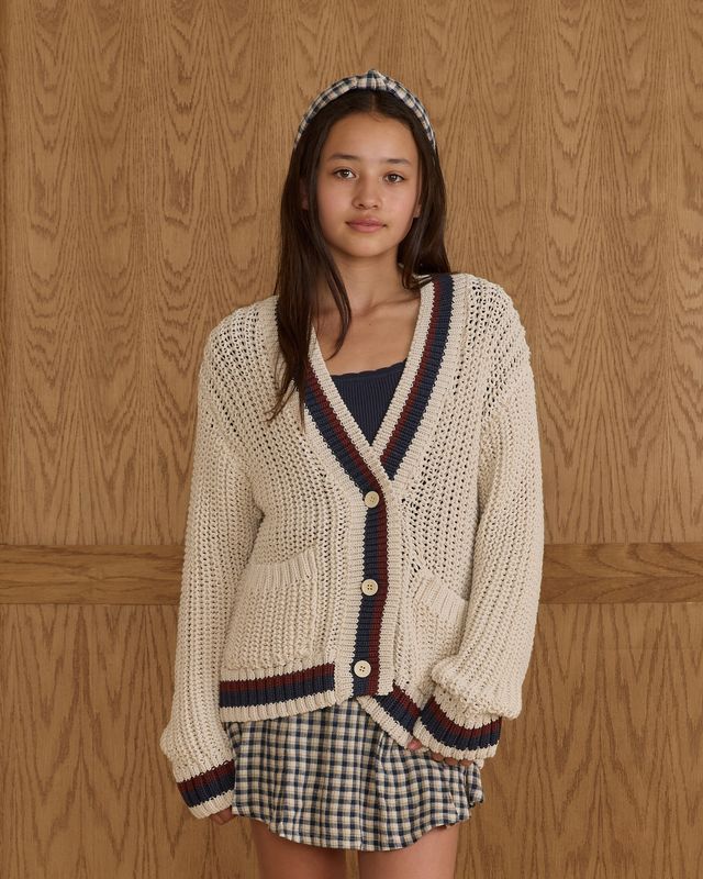 tween girl wearing a long beige cardigan with burgindy and navy stripes on the edges. 