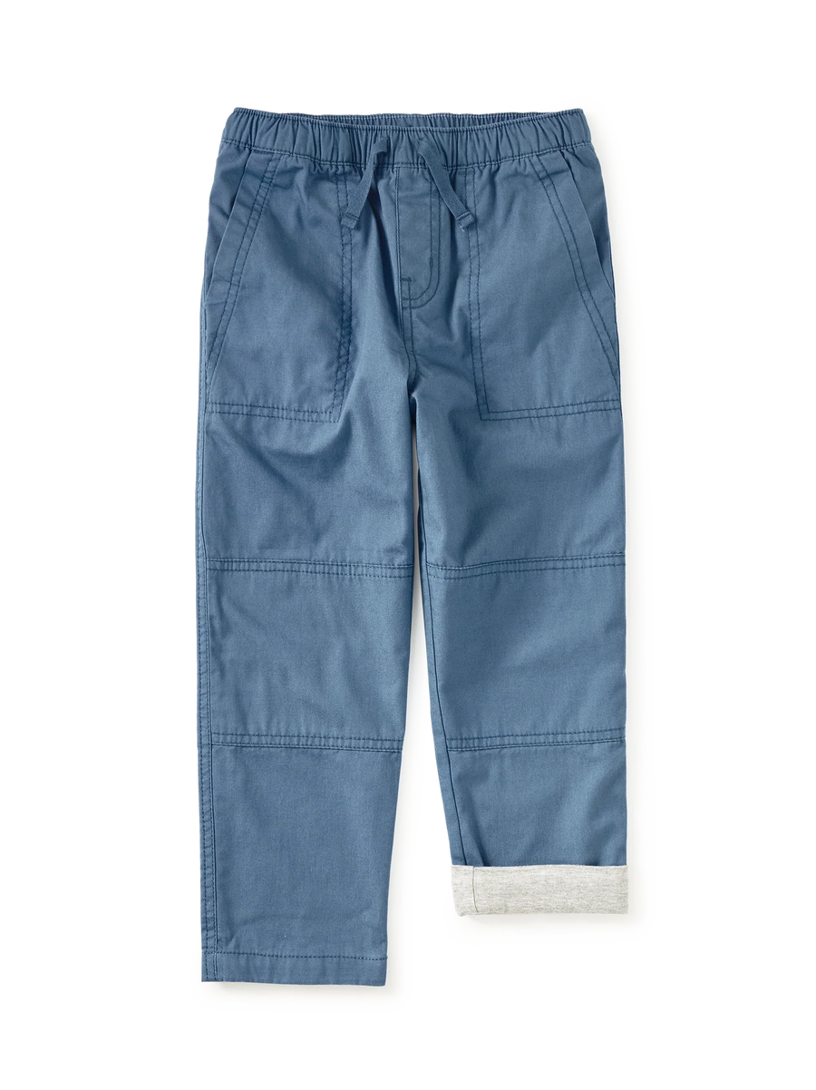 A pair of blue denim-style pants with an elastic waistband, drawstring, large front patch pockets, and a folded cuff showing a light gray inner lining, photographed on a clean white background.