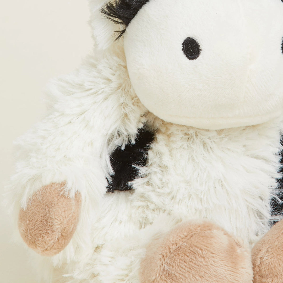 Close-up of a plush cow toy with white fur, black spots, and brown patches.