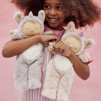 Child holding two plush toys resembling unicorns against a pink background