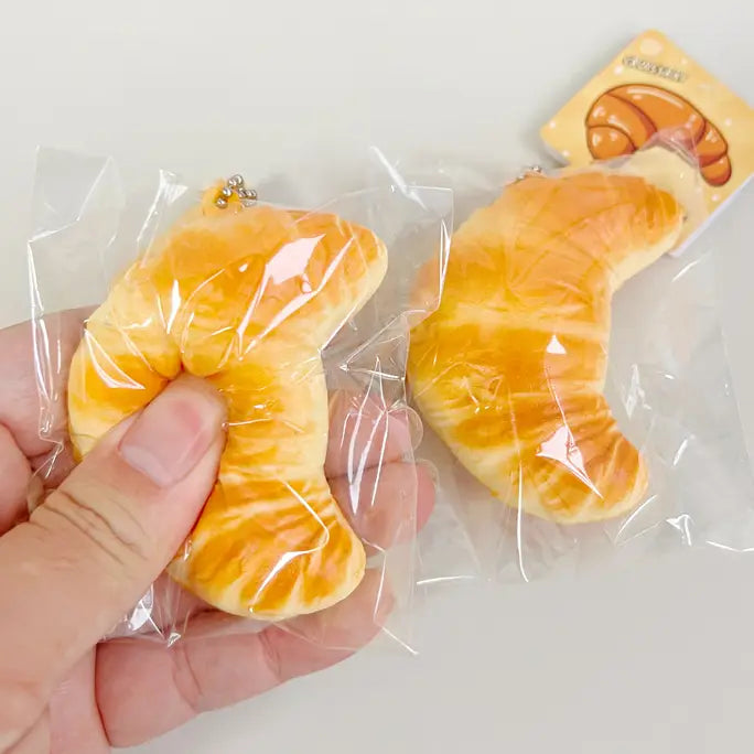 Squishy toy shaped like a croissant held by a hand with packaging in the background.