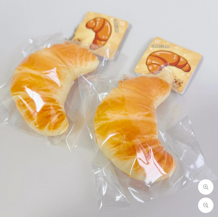 Two croissant-shaped squish toys with packaging on a white background