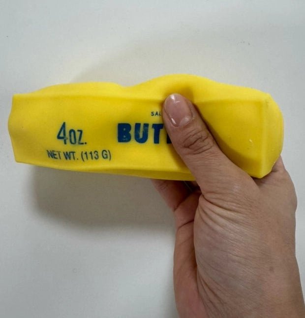 A hand holding a bright yellow 4 oz butter salt block against a plain off-white background.