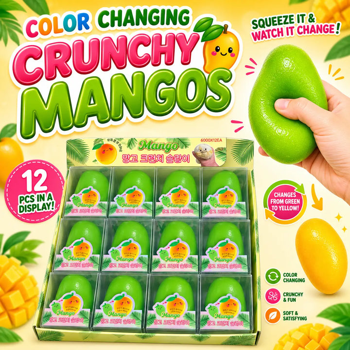 Color changing crunchy mangoes toy set in a clear plastic display box with individual packaged pieces, shown alongside a hand squeezing a green mango-shaped object on a bright yellow background with fruit graphics.