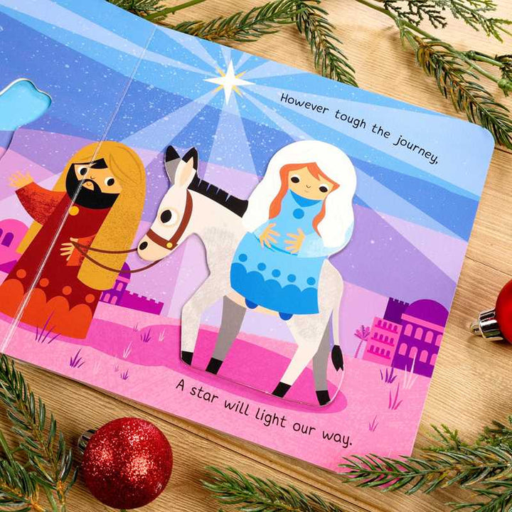 Children's book with illustrations of a man, woman, and horse on a wooden surface with Christmas decorations.
