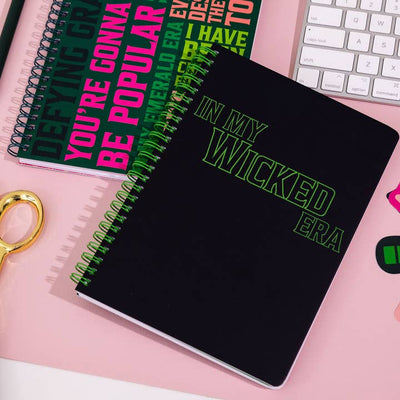 the black notebook with the phrase 'in my wicked era' is on top of the notebook with all the different catch phrases from the musical/movie