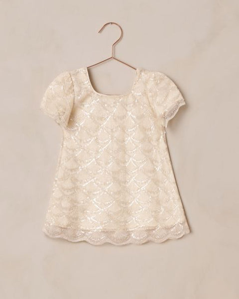 White beaded lace design on a dress on a hanger against a beige background