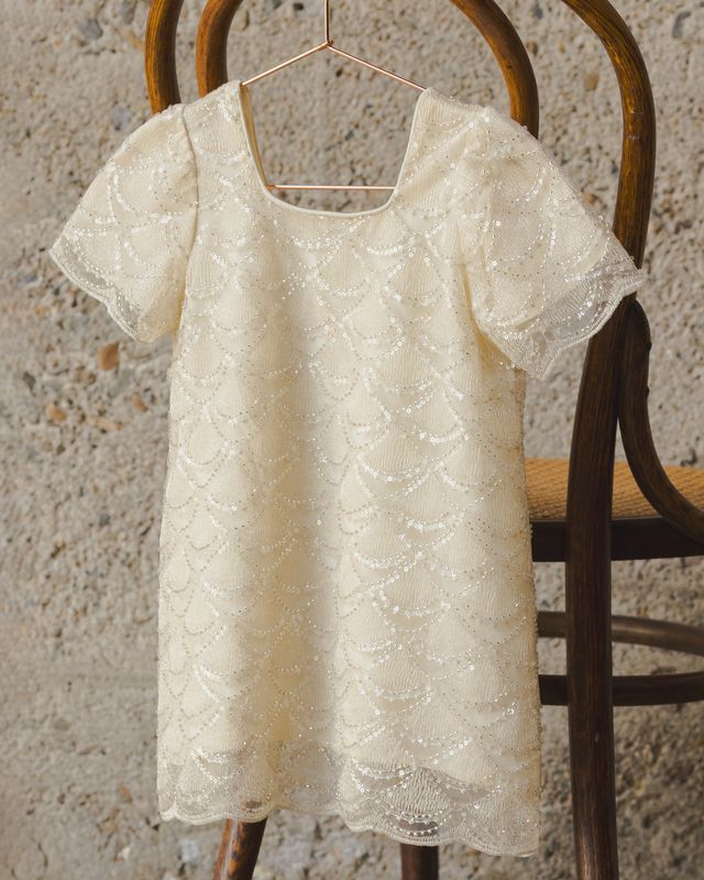 Ivory dress with White lace design beaded top on a wooden chair against a textured wall.