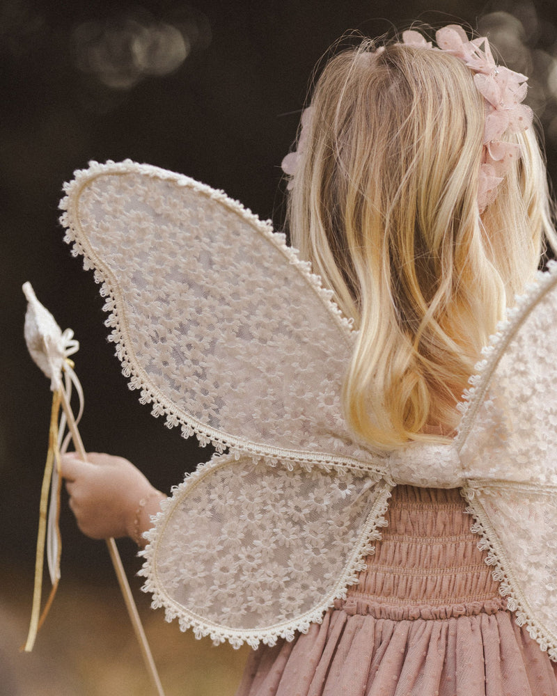 close up of the wings modeled on a young child. The wings have a daisy pattern on them and are beige in color. 