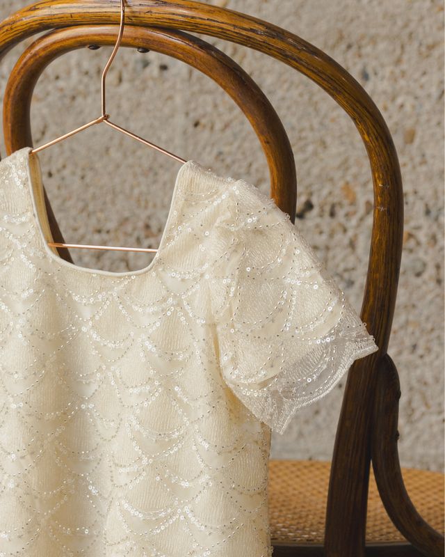 Beige lace top on a hanger against a textured wall.