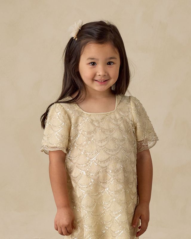 Young girl wearing a beige beaded lace dress against a beige background