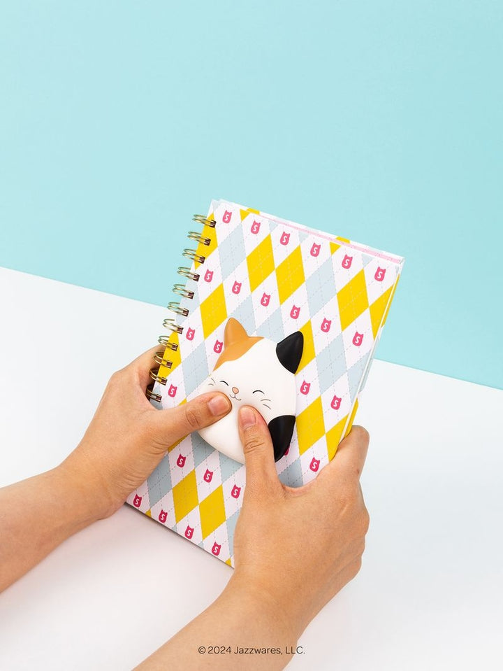 Person holding a spiral-bound notebook with a cat design on a light blue background