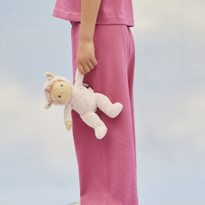 Person wearing pink pajamas holding a plush doll dressed as a unicorn against a light background
