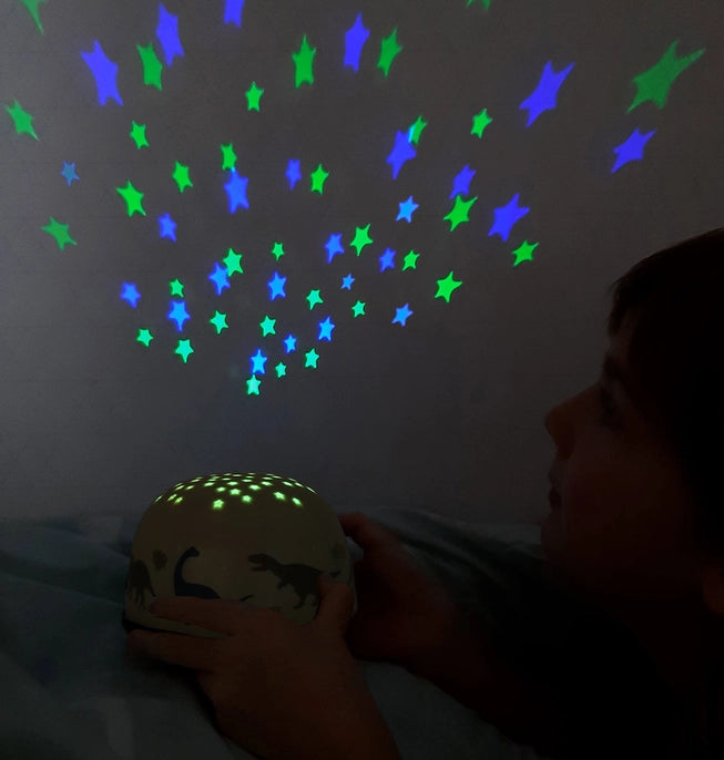 Dinosaur projector light, with little star cut outs on the top of the projector. light comes out blue and green on the wall. This picture demonstrates the light in the night. 