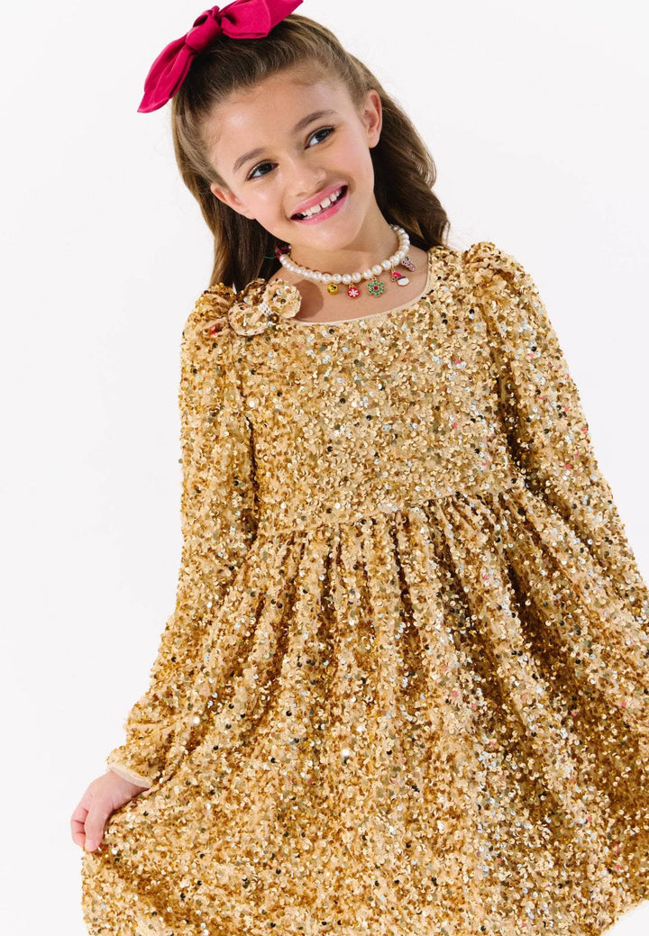 Young girl wearing a gold sequin dress with a pink bow on a white background