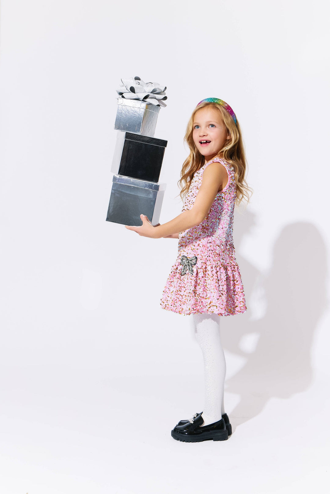 Young girl in a pink sequin dress holding presents against a white background
