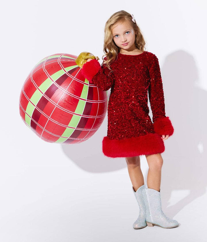 Young girl in a red dress holding a large red and green striped ball on a white background