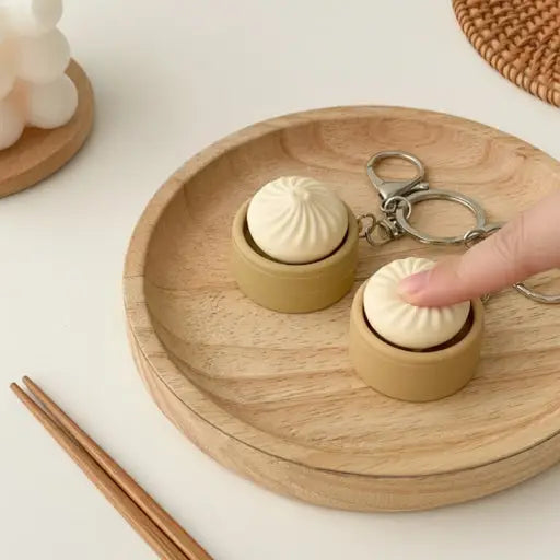 Small wooden containers shaped like dumplings on a wooden plate with a keychain and chopsticks.