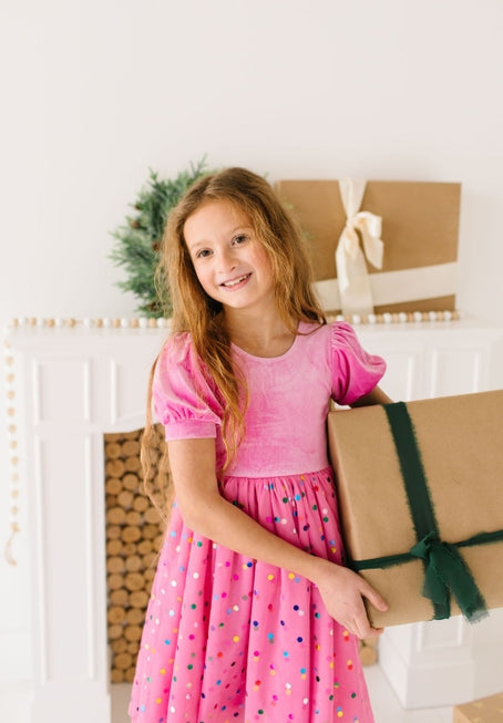 this picture shows the little girl modeling the pink velvet dress and holding a box.  it provides a close up to the texture of fabric on the top and bottom. 