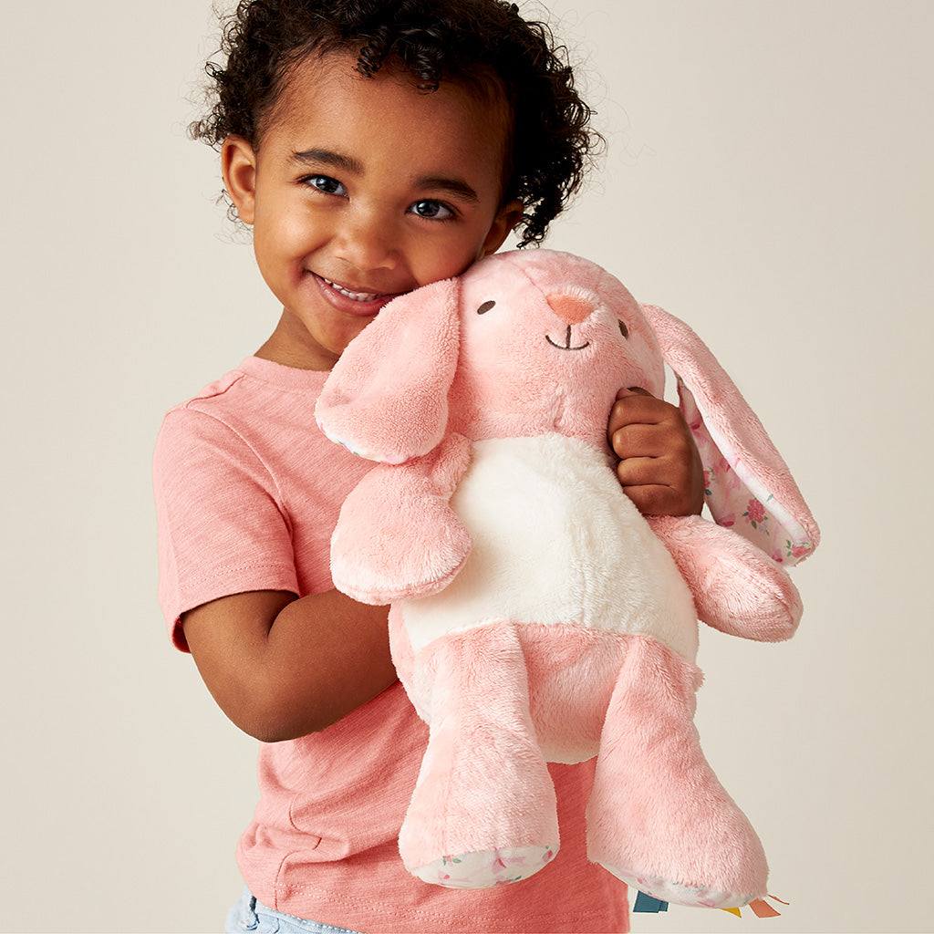 Child holding a pink plush bunny toy against a plain background
