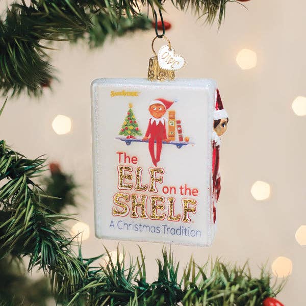 Decorative ornament featuring 'The Elf on the Shelf' with Christmas tree and lights in the background