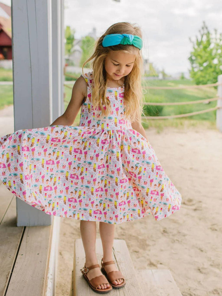 Little girl wearing the ice cream summer printed tank style dress. shes holding out the skirt so you can see the fun print and full skirt option. 