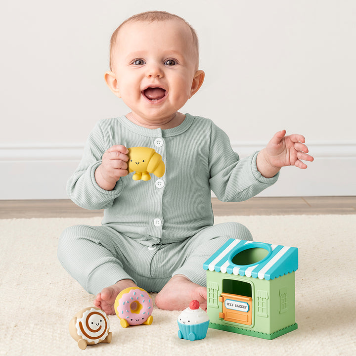 Baby playing with colorful toys on a light wooden floor.