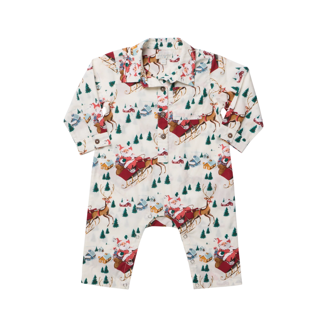 A baby long-sleeve romper with a holiday Christmas print featuring Santa Claus in red sledding, brown reindeer, green pine trees, and snowy houses on an off-white background.