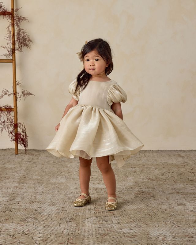 Young girl in a white dress standing on a textured floor with a neutral background