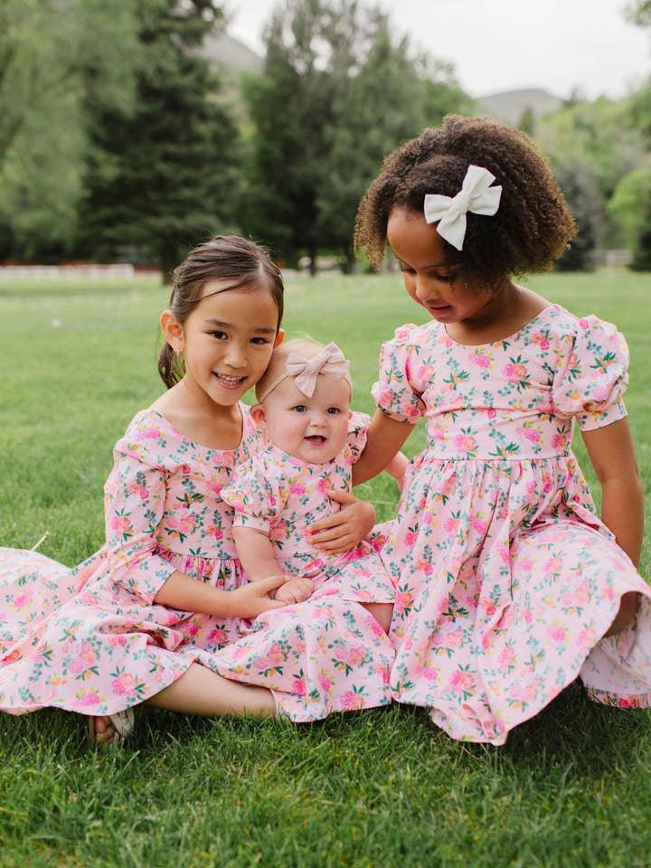 this picture shows a little girl and her friend and small baby all wearing the different styles of the peach bouquet dress. 