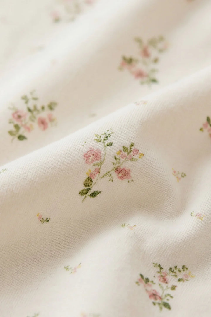Close-up of floral patterned fabric with pink roses and green leaves on a light background
